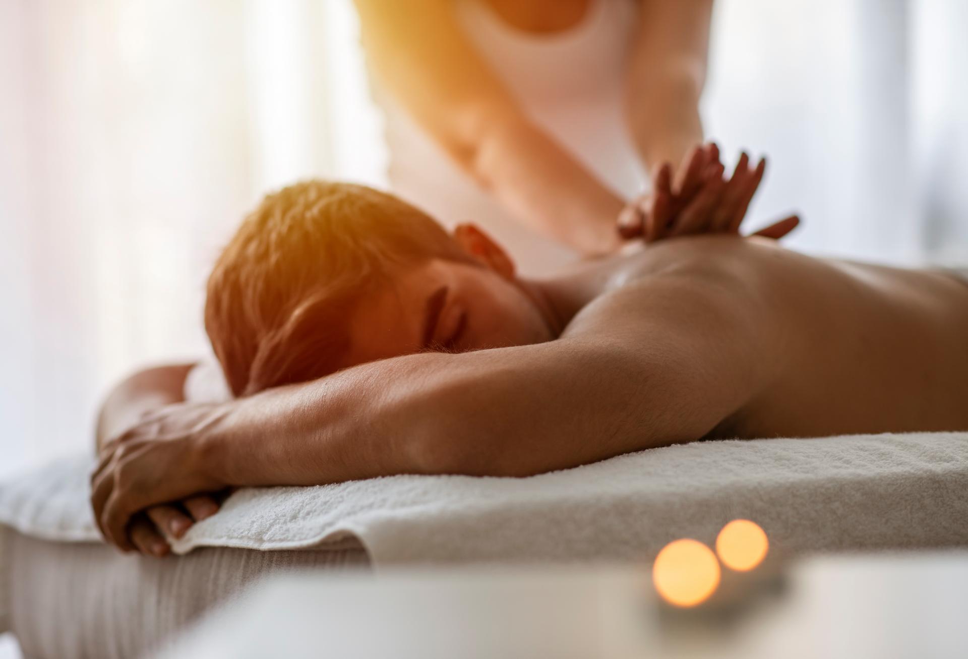 Masseur doing back massage on man's body in the spa salon. Beauty treatment concept. A girl is doing a massage to a guy. Candles in the foreground. Man lying on the table on a white background.